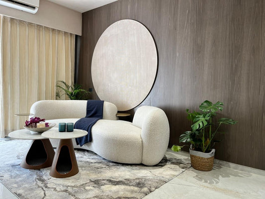 Ambrosia Concepts cream boucle curved sofa with a navy throw, next to a modern coffee table and a large circular wall art.