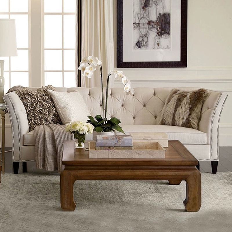 Ambrosia Concepts Old Trafford 3 Seater sofa in neutral fabric with tufted back, nailhead trim, and curved arms. Styled with plush cushions and a throw.